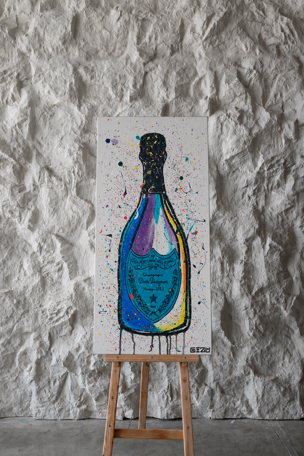 A colorful abstract painting of a champagne bottle on a white canvas, displayed on a wooden easel against a textured white plaster wall.